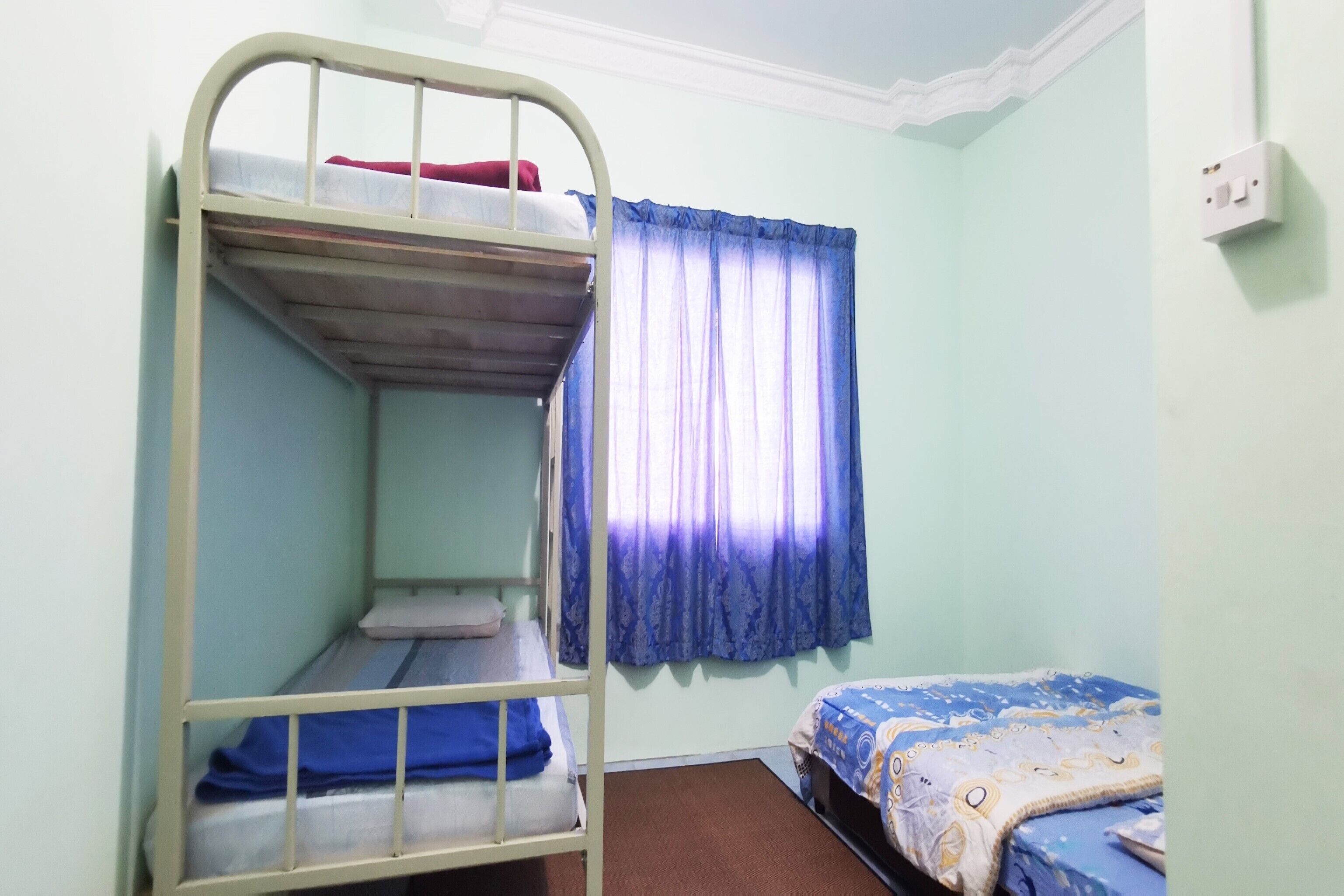 Un dormitorio con literas, una ventana con cortinas azules y un enchufe en la pared.