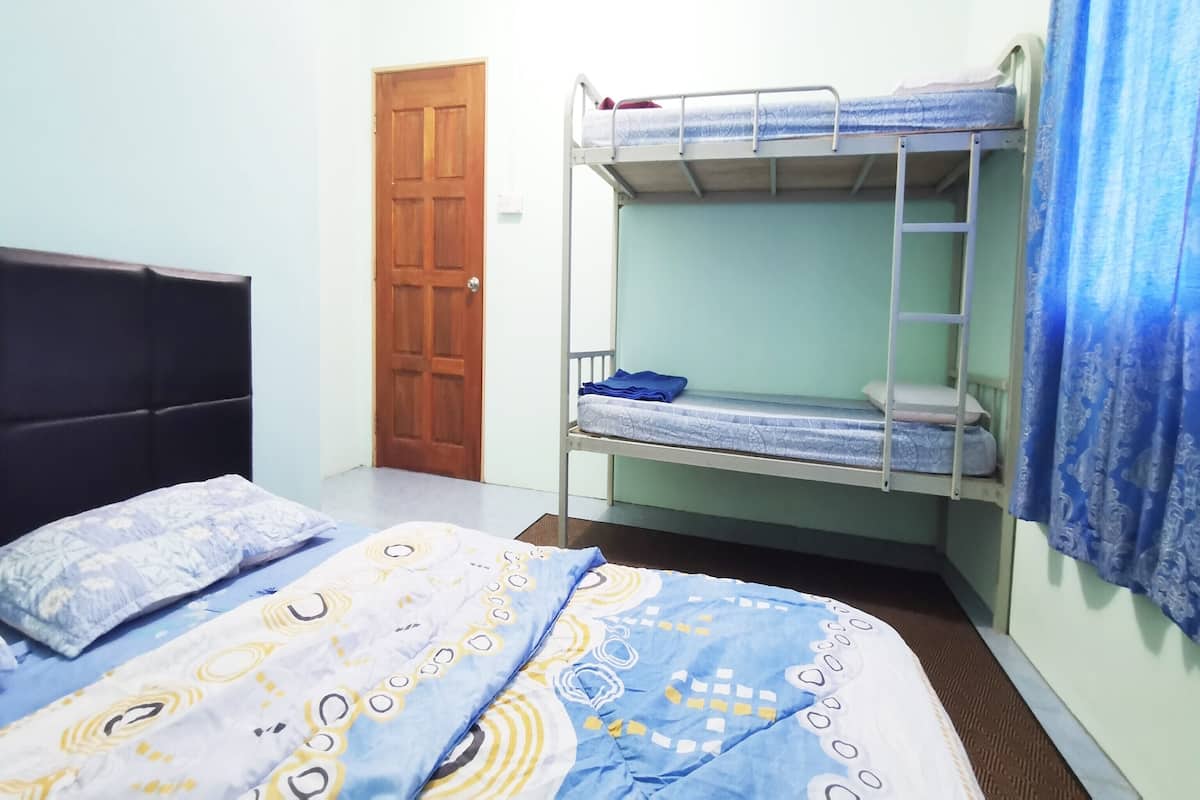 A bunk bed room with a wooden door, a single bed with patterned bedding, and a blue curtain.