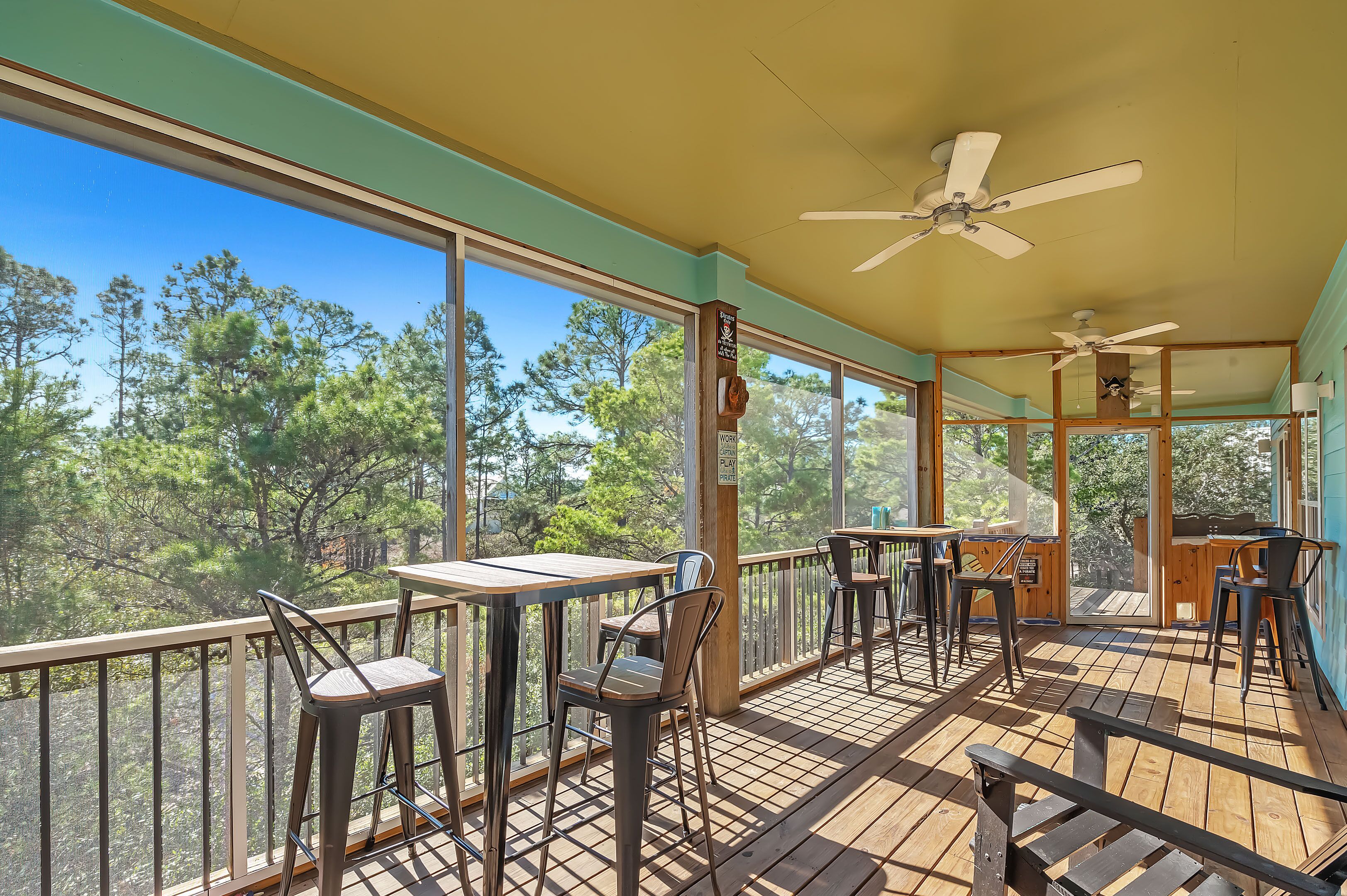 A covered outdoor area with tables and chairs, large windows, and ceiling fans.