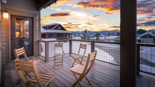 A wooden deck with four wooden chairs and a glass door leading to a room.
