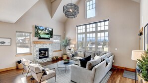 A spacious living room with a fireplace, large windows, and a high ceiling.