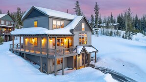 A two-story house with a balcony and a covered porch, surrounded by snow and trees.