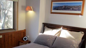 A bedroom with a wooden headboard, a bedside table with a clock, a lamp, and a framed picture on the wall. - Wallace's-Chalet (Dinner Plain)