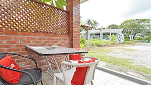 A patio with a table and chairs, a brick wall, and a view of a building in the background. - Hotel O Inspire Rooms (Langkawi)