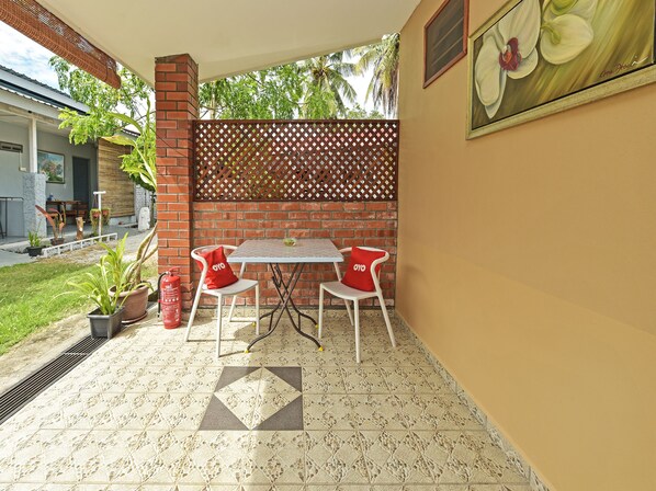 Un patio con una mesa, dos sillas, un muro de ladrillo, un panel de celosía y una planta en maceta.