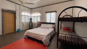 Une chambre avec un lit superposé, un lit simple, un ventilateur de plafond et un tapis rouge à motifs.