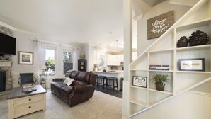 A living room with a brown leather sofa, a coffee table, and a bookshelf with framed items and books.