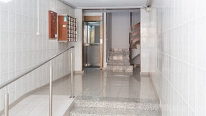 A clean, modern interior with a tiled wall, a metal handrail, and a staircase leading to an elevator.