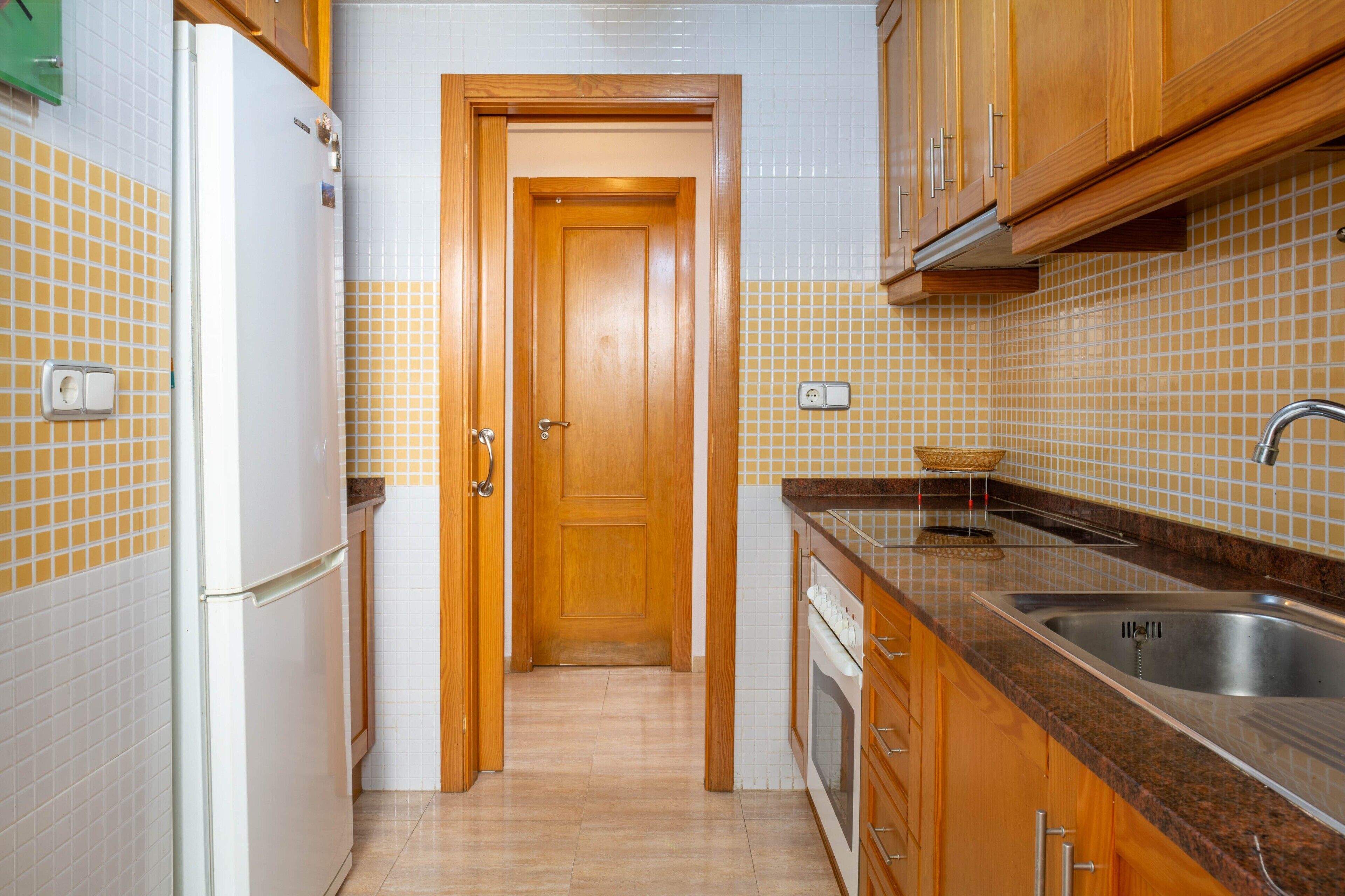 Una cocina con armarios de madera, un lavamanos de acero inoxidable, un refrigerador blanco y salpicadero de azulejos.
