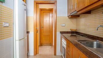 Una cocina con armarios de madera, un lavamanos de acero inoxidable, un refrigerador blanco y salpicadero de azulejos.