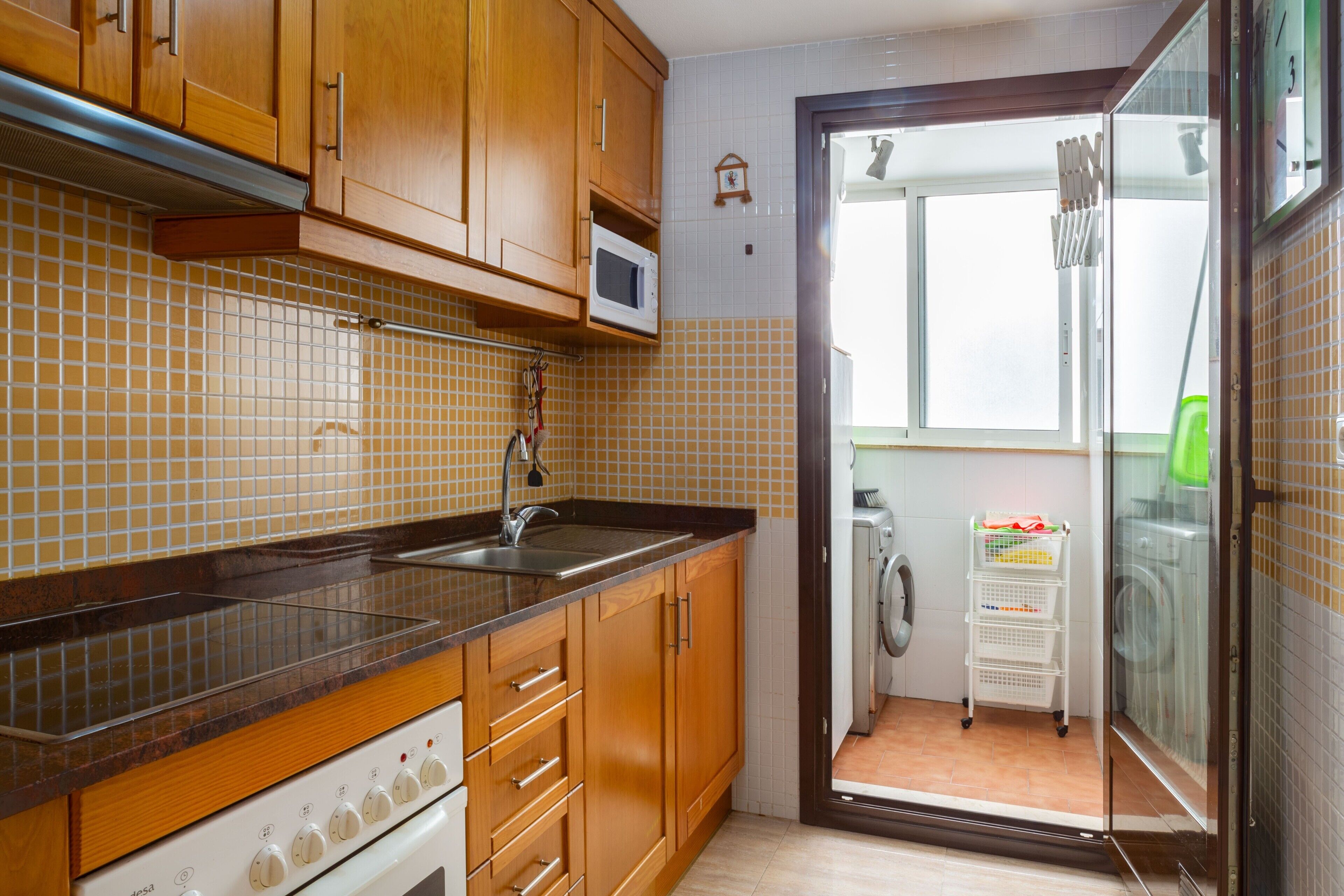 Una cocina con armarios de madera, un microondas, un fregadero y vistas a un área de lavandería.
