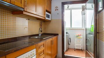 Una cocina con armarios de madera, un microondas, un fregadero y vistas a un área de lavandería.
