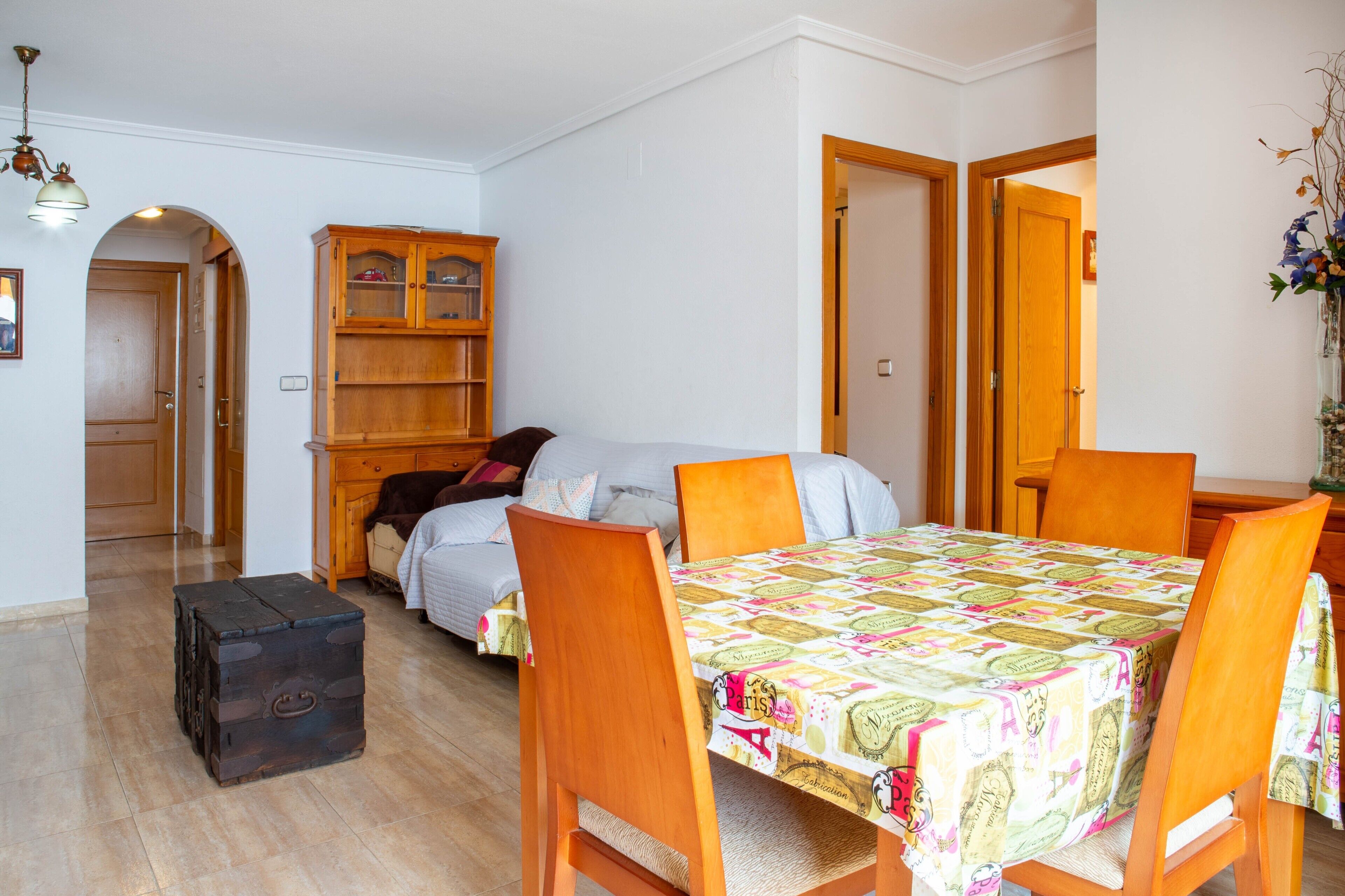 Een kamer met een houten eettafel, stoelen, een bank, een kast en een koffer.