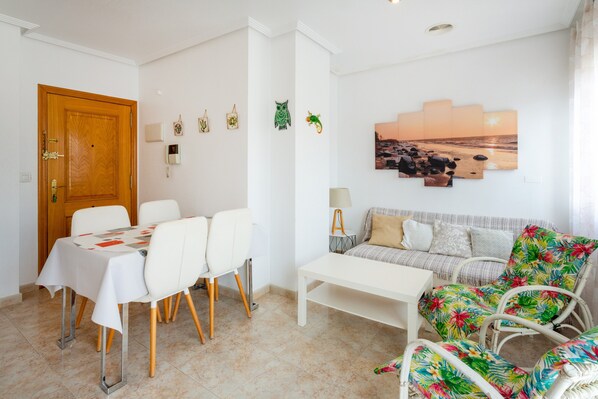 A dining area with a table and chairs, a sofa, and a wall with a sunset painting.