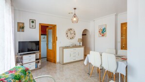 A living room with a TV, dining table, chairs, a cabinet, and a clock.