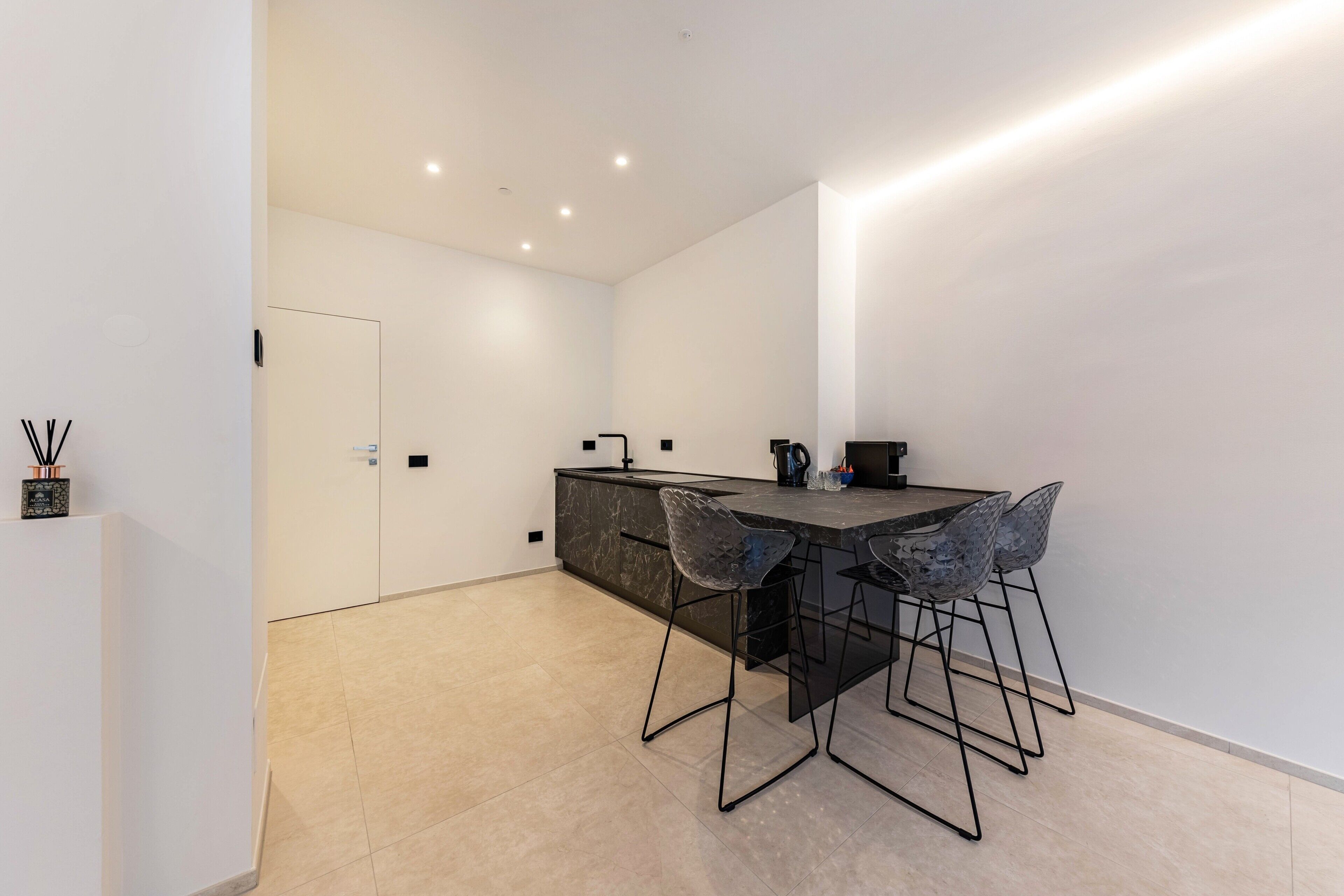 A modern kitchen with a dark countertop, a black chair, and a white door.