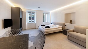 Un dormitorio moderno con cama, sofá, televisión y mesa de comedor.