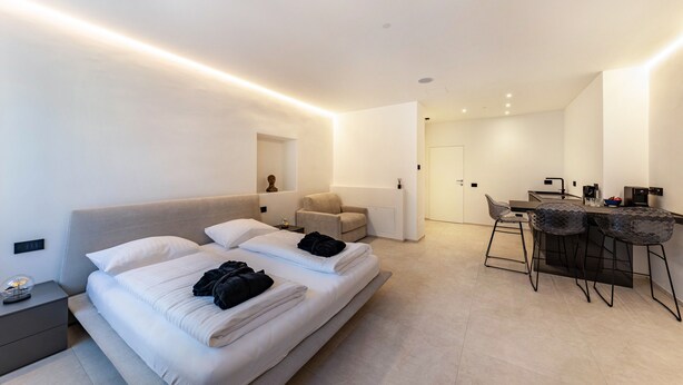 Una habitación de hotel moderna con cama, mesita de noche, silla, escritorio y zona de bar.