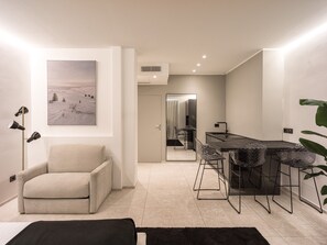 A modern living room with a sofa, a dining area with bar stools, a large mirror, and a painting of a snowy landscape.