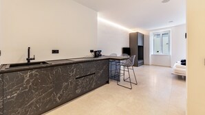 Una cocina moderna con una isla de mármol, taburetes de bar y un sofá blanco en una sala de estar luminosa.