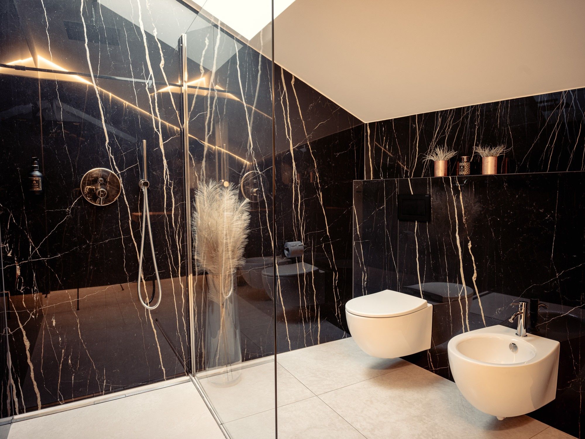 Ein modernes Badezimmer mit schwarzen Marmorwänden, einer Duschkabine aus Glas, einem Bidet und einem Waschbecken.