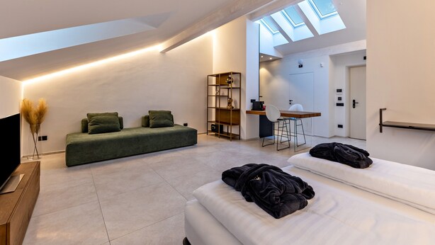 A modern loft bedroom with a skylight, a green sofa, a white bed, and a small desk area. - Studio Apartment 'App 303 Palazzo Cavour' with Mountain View, Wi-Fi and Air Conditioning (Bolzano)