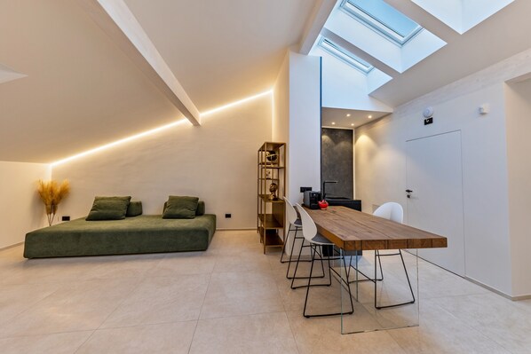 A modern loft bedroom with a skylight, a green sofa, a wooden dining table, and a minimalist decor.