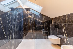 A modern bathroom with a glass partition, marble walls, and a skylight.