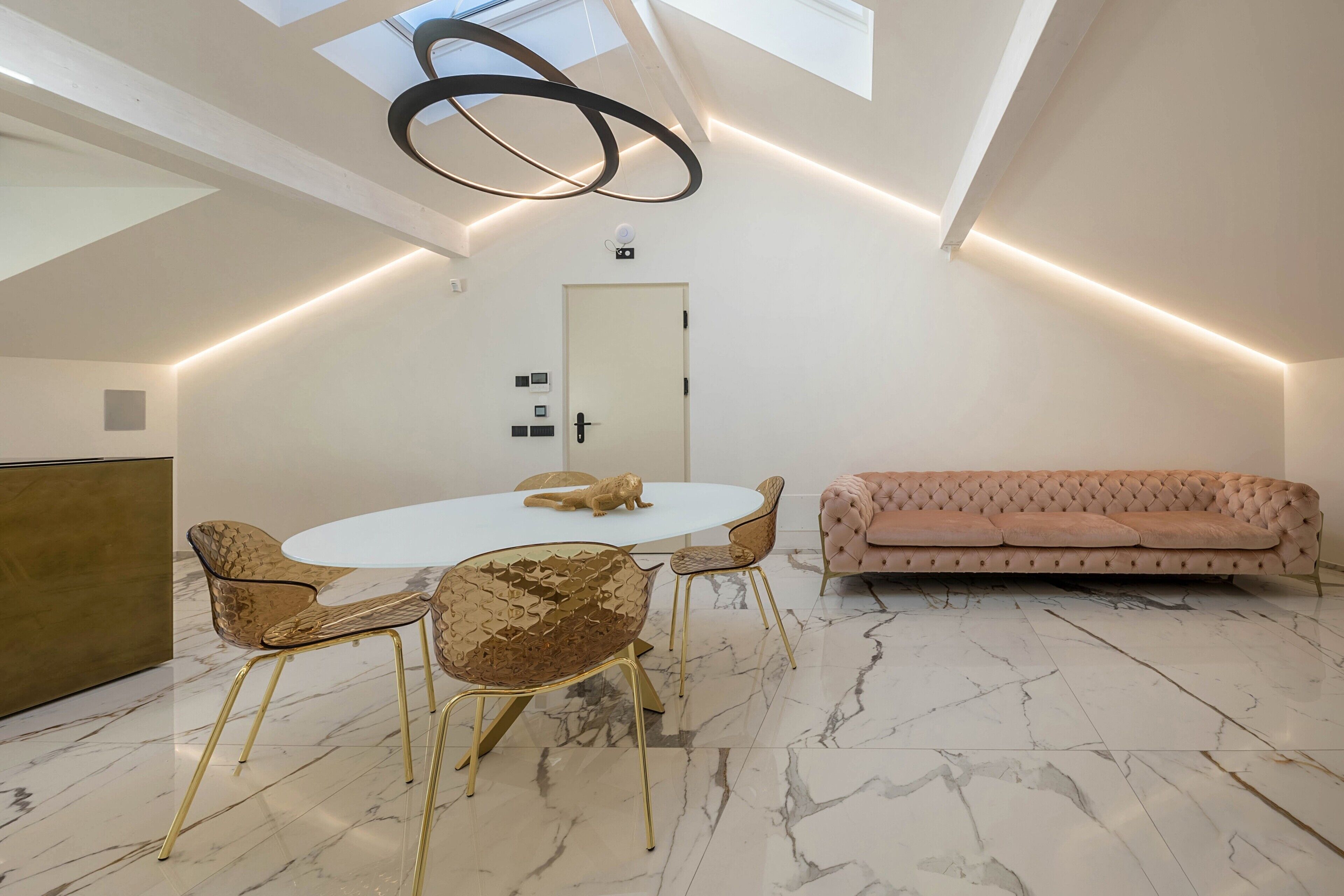 Un espace repas moderne avec une table ronde, des chaises dorées et un canapé rose.