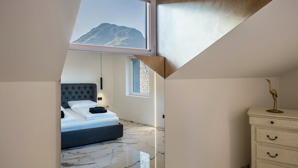 Een slaapkamer met een bed, een dressoir, een nachtkastje, een raam met uitzicht op bergen en een dakraam.