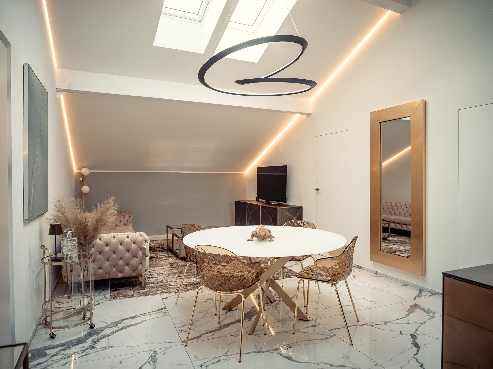 Un espace repas moderne avec une table ronde, des chaises dorées et un canapé capitonné.