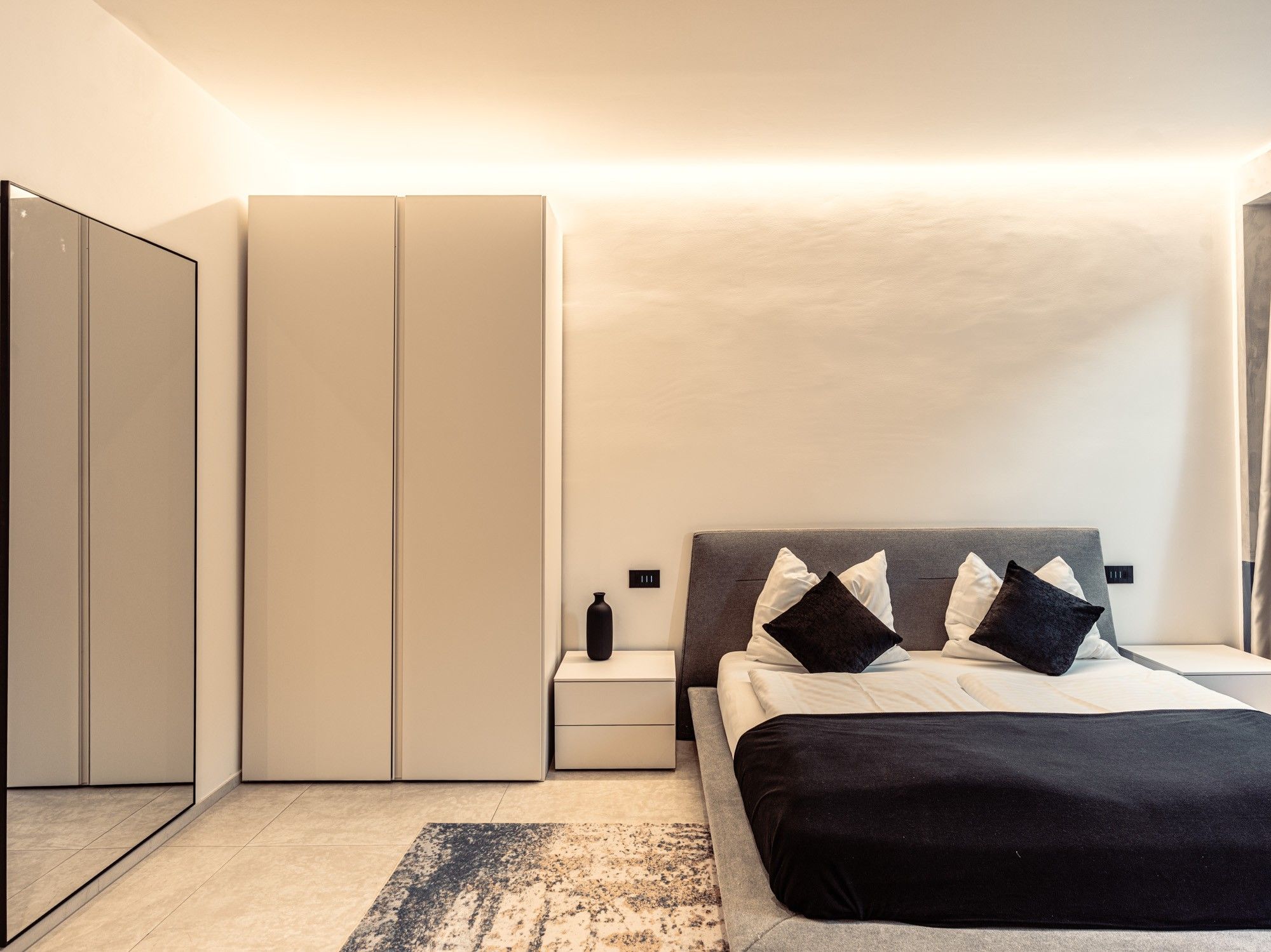 A modern bedroom with a bed, nightstands, a wardrobe, and a rug.