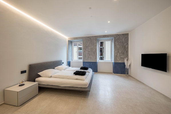 Une chambre à coucher moderne avec un lit, des tables de chevet, une télévision et une fenêtre.