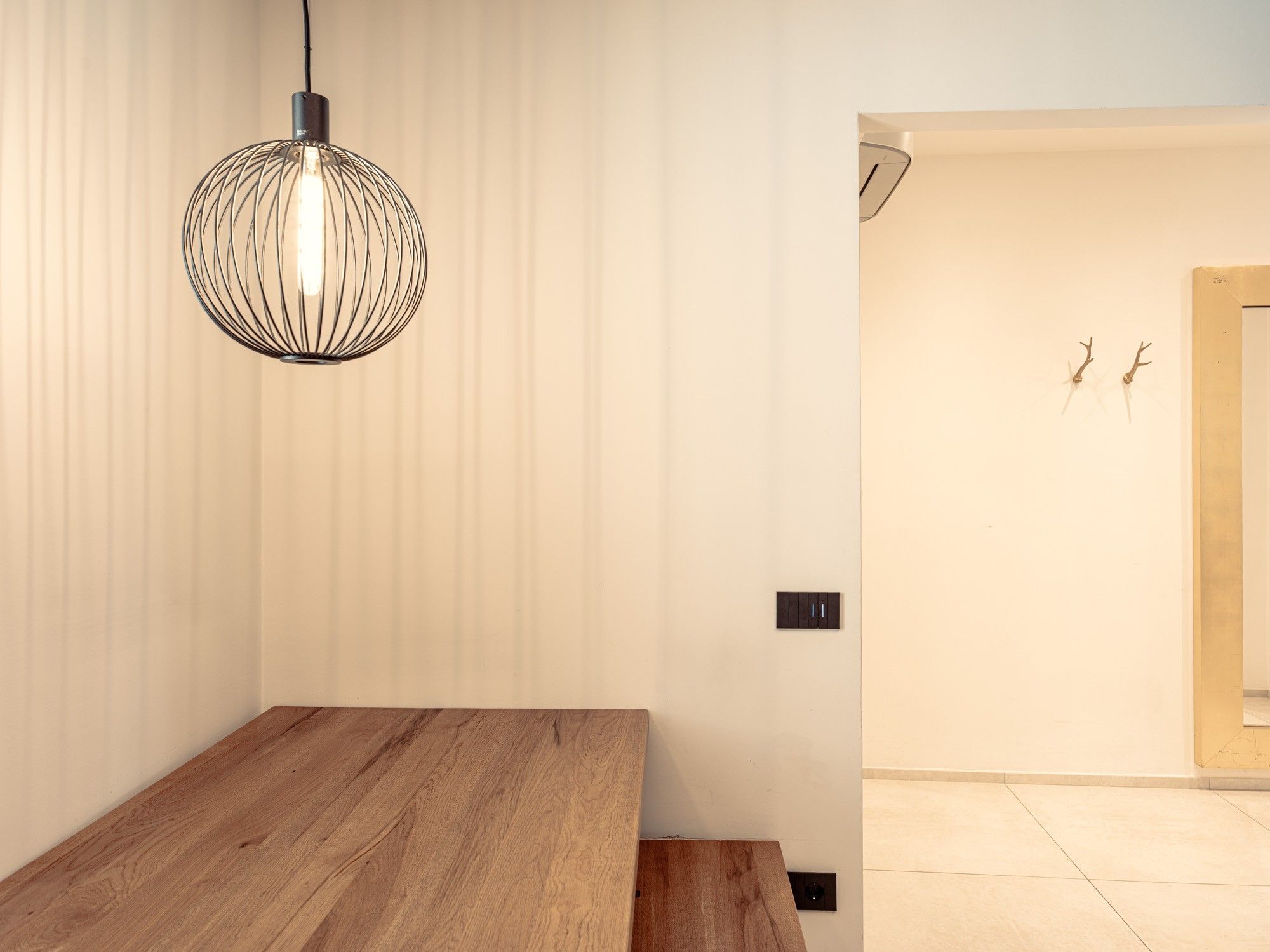 Un intérieur moderne avec une table en bois, un luminaire suspendu et un mur sobre agrémenté d’une porte.