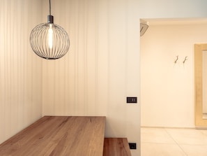 Un intérieur moderne avec une table en bois, un luminaire suspendu et un mur sobre agrémenté d’une porte.
