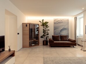 A modern living room with a wooden cabinet, a brown leather sofa, a large potted plant, and a wall-mounted TV.