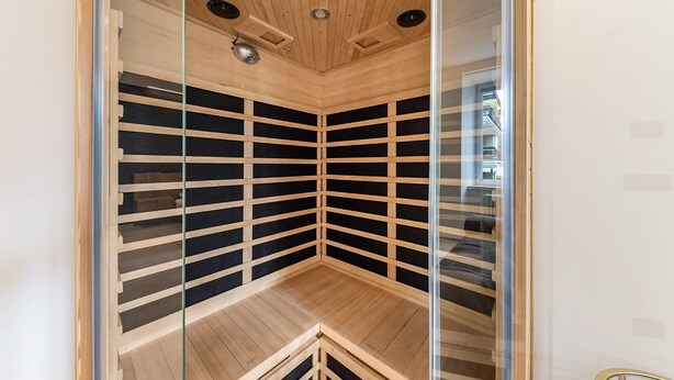 Una sala de sauna con techo de madera, paredes de vidrio y un banco.