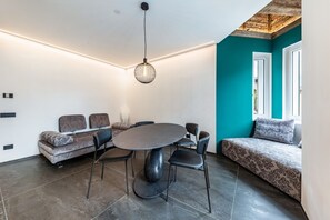 Un salon moderne avec une table ronde, un canapé et des fauteuils, un luminaire suspendu et un mur d’accent de couleur turquoise.