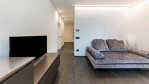 A modern living room with a flat-screen TV, a sofa with patterned cushions, and a minimalist design.
