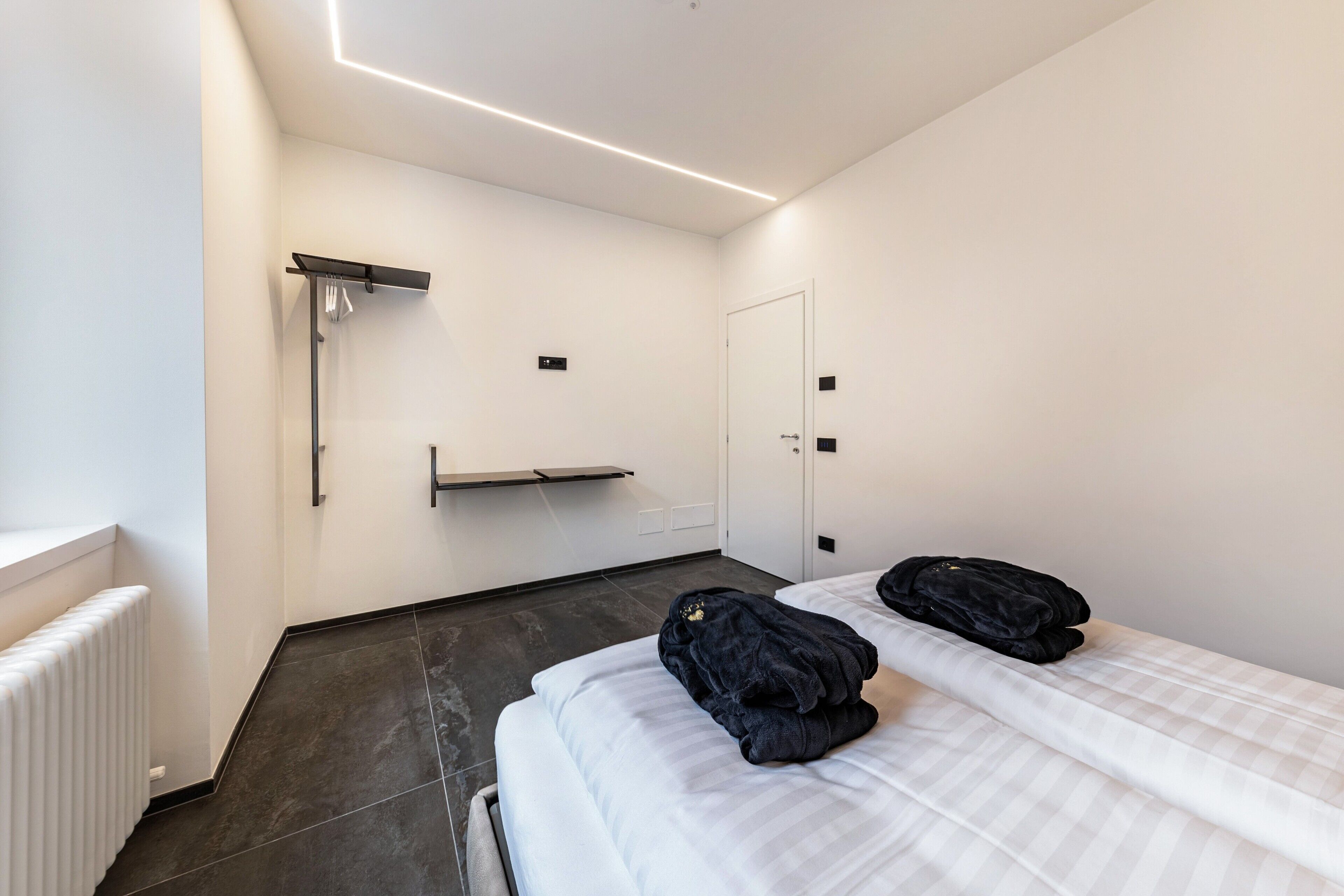 Ein modernes Hotelzimmer mit Bett, Heizkörper, Handtuchhalter und Tür.