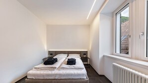 A modern bedroom with a large bed, bedside tables, a window, and a radiator.