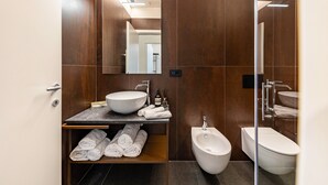 A modern bathroom with a large mirror, a vessel sink, a bidet, and neatly folded towels.