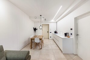 Une cuisine moderne avec des meubles blancs et un plan de travail, un coin repas avec une table et des chaises en bois, et un couloir avec une porte donnant sur une autre pièce.