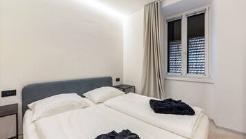 A hotel room with a bed, a bedside table, a window with blinds, and a curtain.
