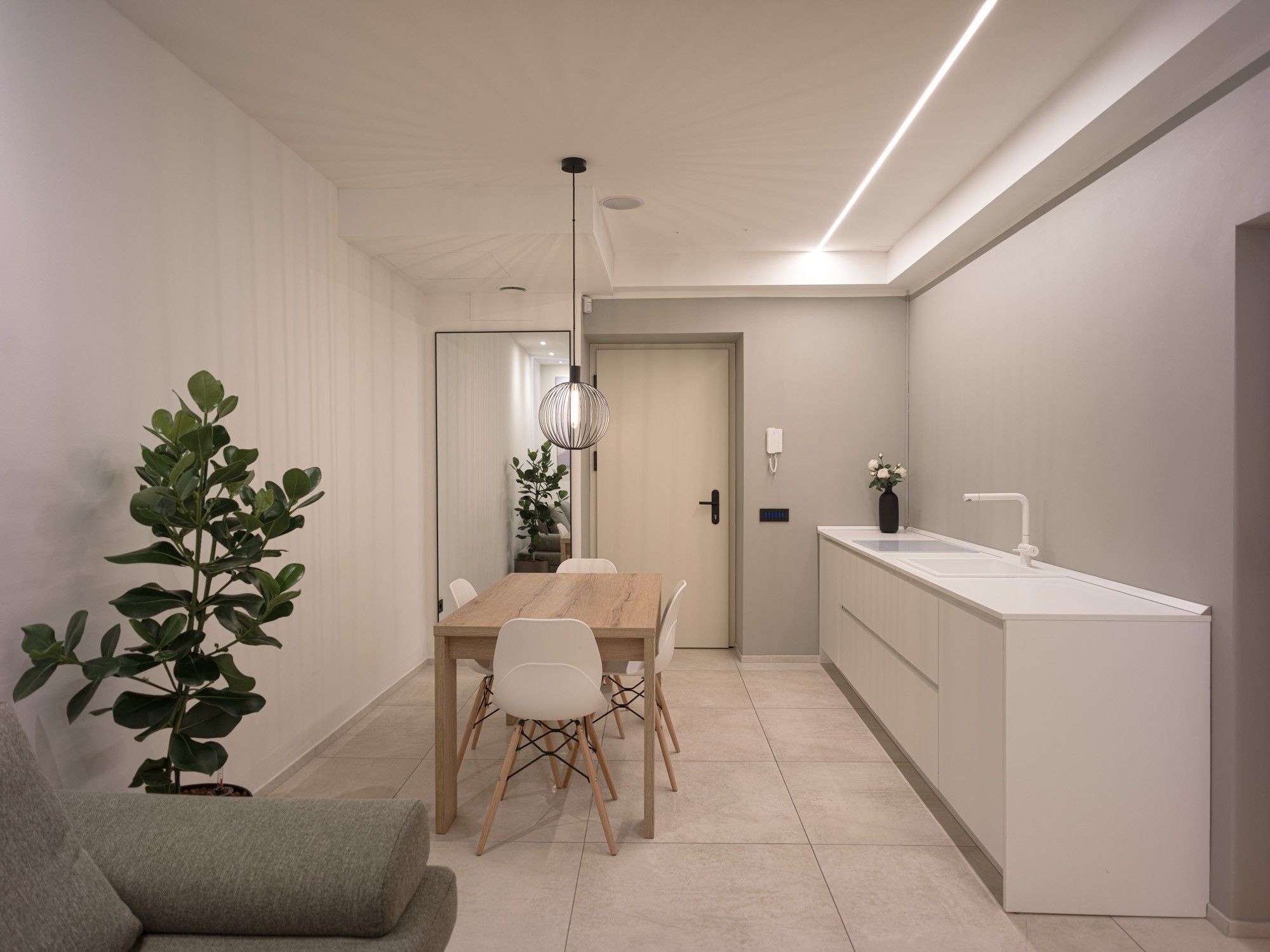 A modern kitchen with a wooden dining table and chairs, a white countertop, and a hanging pendant light.