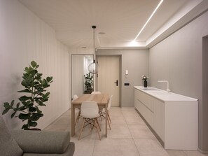 Een moderne keuken met een houten eettafel en stoelen, een wit aanrechtblad en een hangende hanglamp.