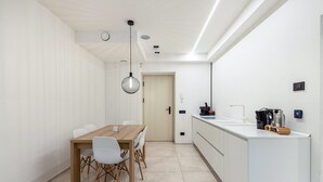 A modern kitchen with a wooden dining table, white chairs, and a hanging light fixture.