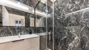 A modern bathroom with a marble wall, a glass shower enclosure, and a vanity with a mirror.