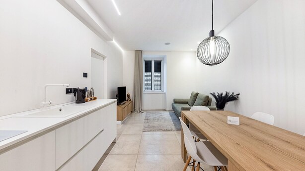 A modern kitchen with a white countertop, a wooden dining table, and a hanging light fixture.