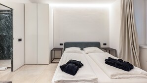 A modern hotel room with a bed, bedside tables, a wardrobe, and a bathroom with a marble wall.